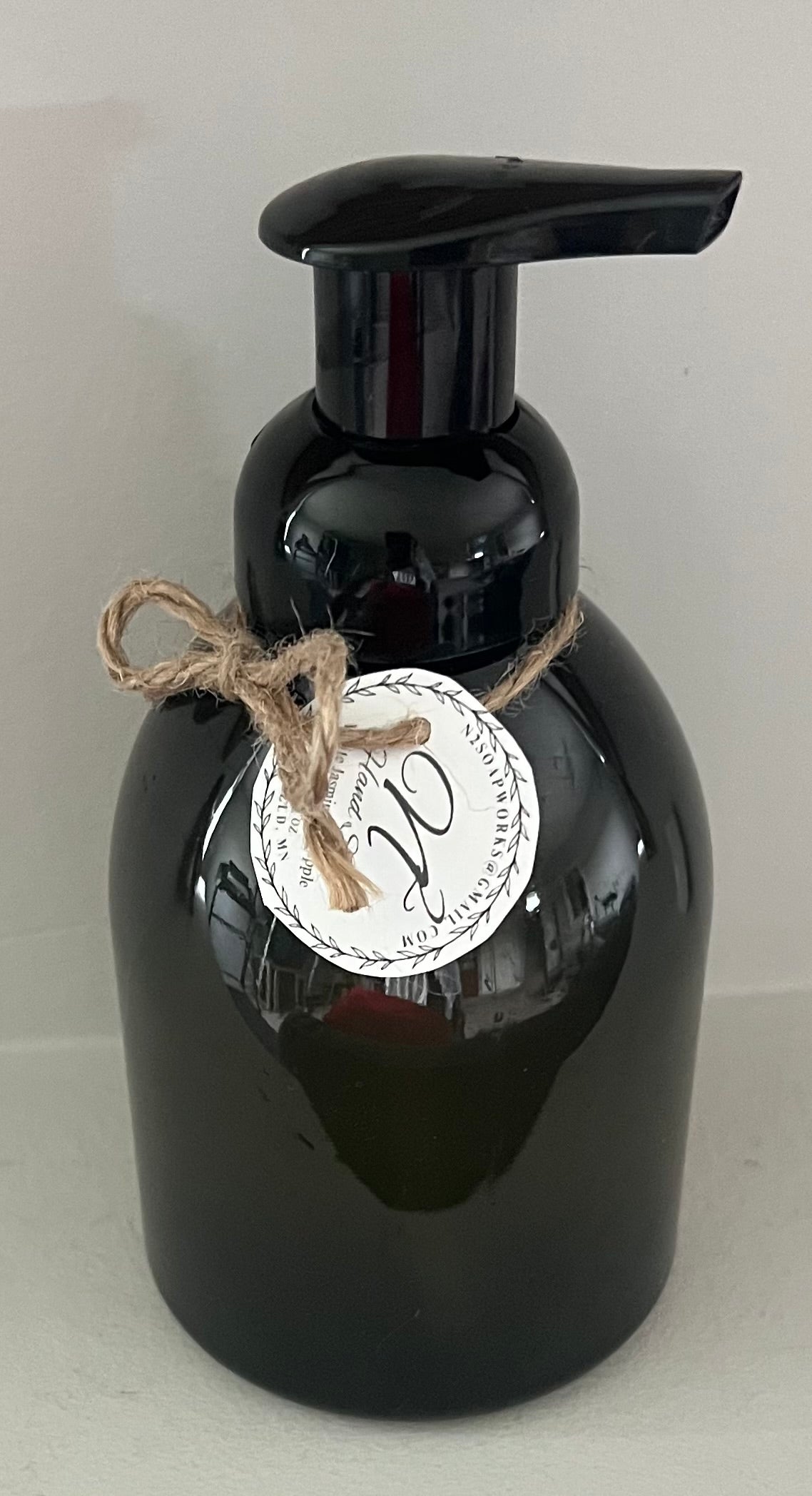 Black soap dispenser with a label and string on a light gray background